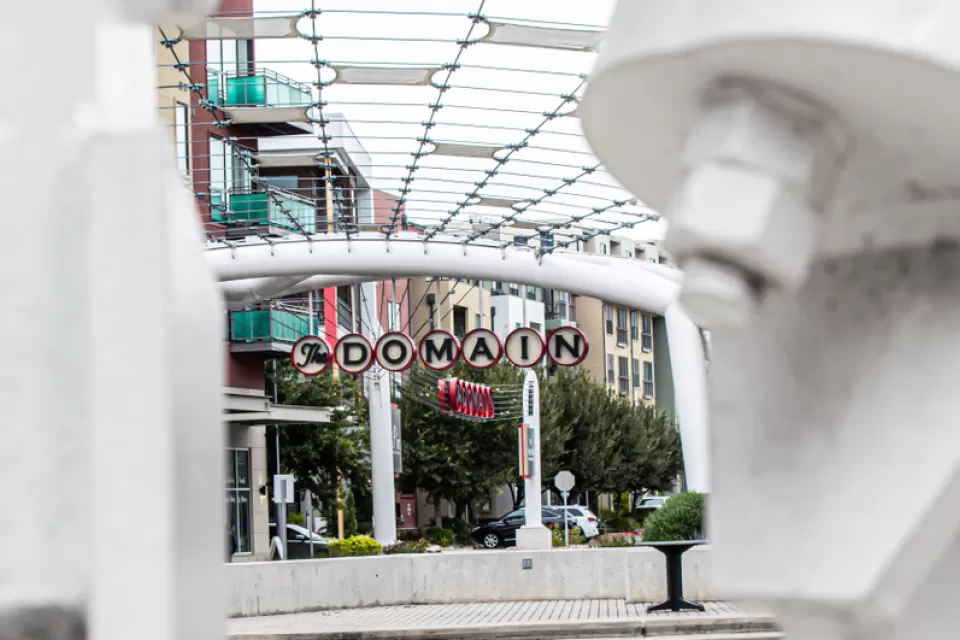 A picture of a decorative sign announcing “The Domain” surrounded by high density shops and apartments.